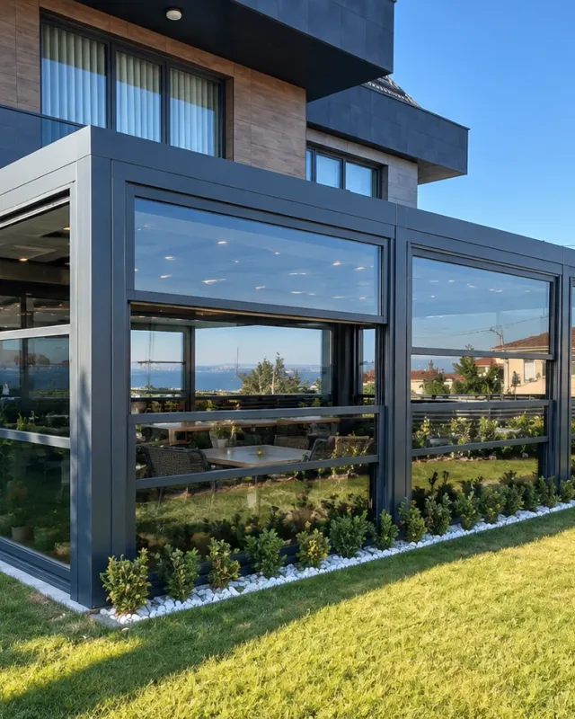 Giyotin cam sistemi, bahçeli modern villanın köşe camlı eklentisinde üst panelin yukarı kaldırılıp altında açık bir boşluk bıraktığı, gün ışığında dış mekândan görünüm