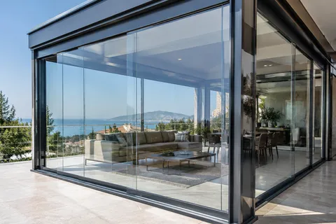 Sürme cam balkon sistemi, panellerin yatay ray üzerinde hareket ettiği köşe uygulaması, deniz manzaralı teras